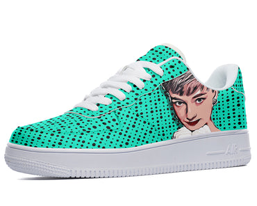 A close-up of a sneaker with a green and white polka dot pattern. The sneaker has a white sole and white laces. The face of a woman with short dark hair is depicted on the side of the shoe.