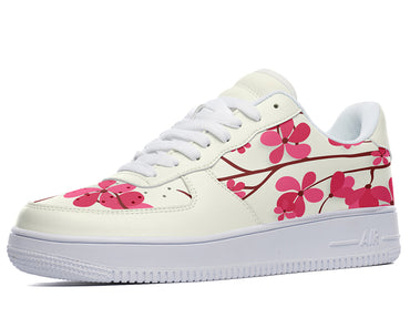 A white sneaker with a pink floral pattern. The sneaker is low-top and has a white sole. The floral pattern is of pink cherry blossoms.