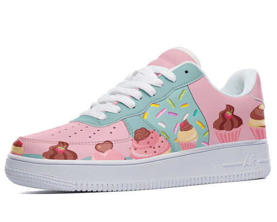 A close-up of a sneaker with a light pink upper and white sole. The upper is decorated with colorful sprinkles, cupcakes, and hearts.