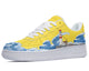 A yellow sneaker with a white sole and white laces. The sneaker has a design of a lighthouse on a rocky cliff with blue waves crashing against it.