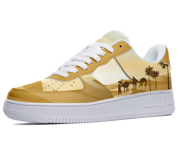 A yellow sneaker with a white sole and white laces. The design on the shoe is a desert scene with a camel train and palm trees.