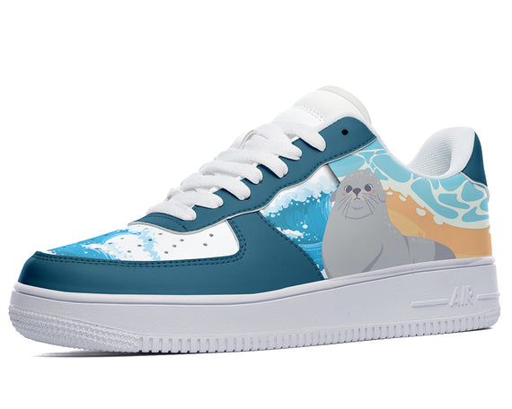 A blue and white sneaker with a cartoon seal on the side. The seal is gray and has a black nose. It is standing on a beach in front of a wave. The sneaker has a white sole and white laces.