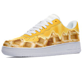 A yellow sneaker with a white sole and white laces. The sneaker has a design of dripping melted butter and waffles.